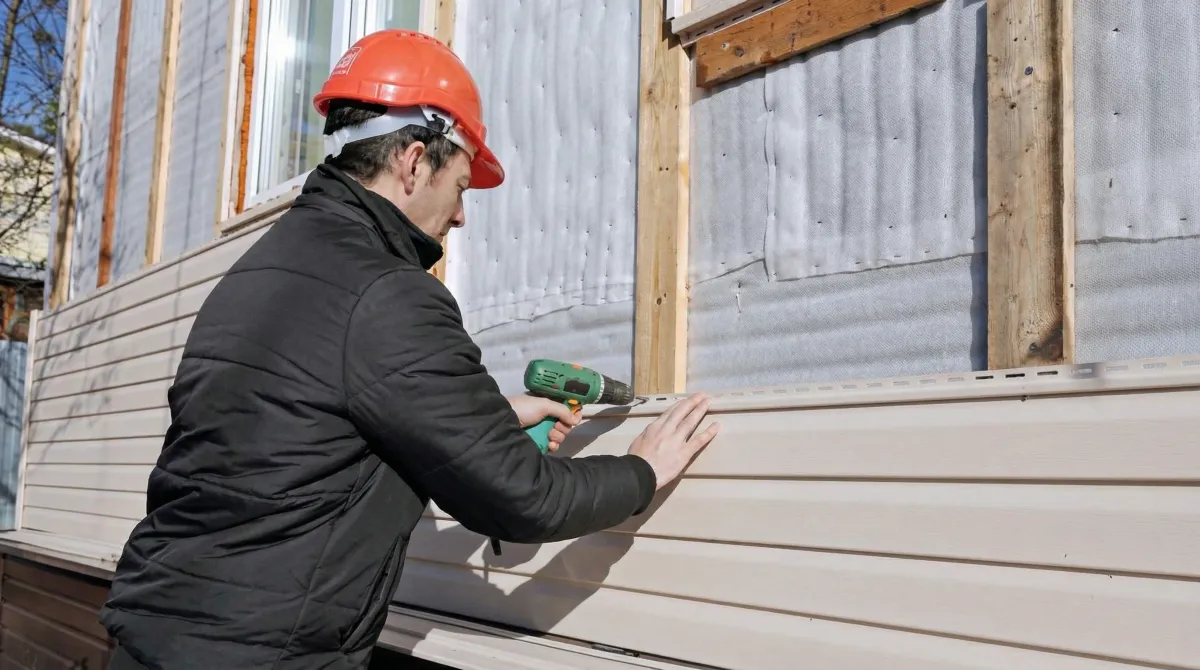 Siding replacement professional using a power drill to install new tan vinyl siding on a home exterior in South Bend, IN